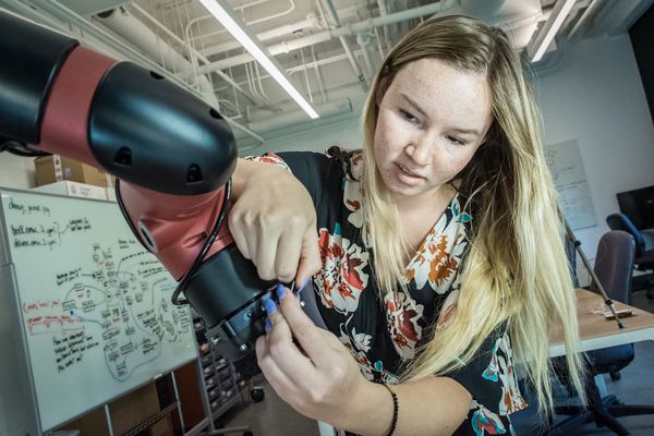 A student working on the wrist of a red robot arm in the lab